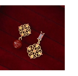 Macro shot of asymmetric gold hollow flower earrings with red beads on velvet