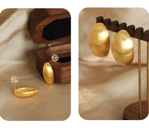 Detail of matte gold oval stud earrings on champagne silk background with jewelry stand