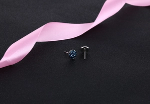 Close-up of round dark blue crystal cluster stud earrings with silver pins on black fabric