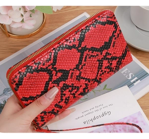 Red snakeskin textured long wallet with golden zipper and wristlet on a wooden table