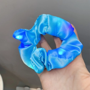 Detailed view of hand-held blue LED glowing satin scrunchie for ponytail hairstyles