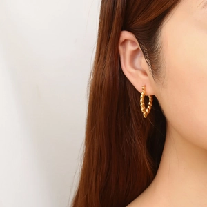 Detail of vintage gold C-shape hoop earrings with textured beaded pattern on a female model