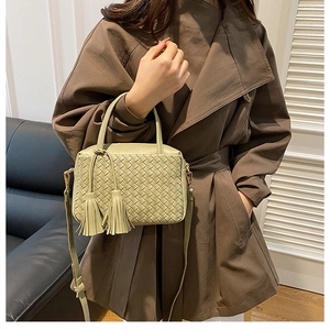 Detail of woven sage green crossbody bag shown on model in a cozy indoor setting