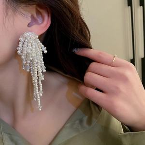 Détail de longues boucles d'oreilles à pompons avec perles blanches et cristaux