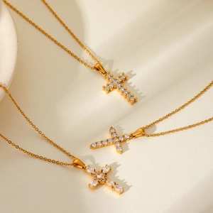 Golden cross pendant necklace with sparkling cubic zirconia on a beige stone surface