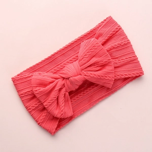 Detail of coral pink knitted baby headband featuring a large bow and soft cable texture