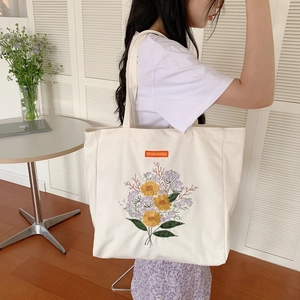 Close-up of floral embroidery detail on cream canvas tote bag with sunflower patterns