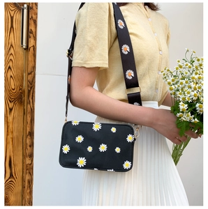 Detail of black crossbody bag with white daisy prints and adjustable gold hardware