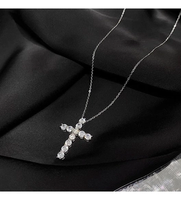 Detailed close-up of a silver cross necklace with clear zircons on black silk fabric