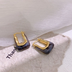 Detailed shot of U-shaped gold earrings with purple marble resin on artistic paper