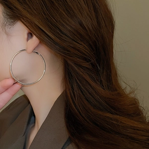 Close-up of a large polished silver hoop earring worn by a model in a professional setting