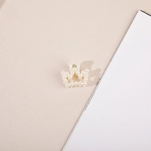 Close-up of a small crown-shaped hair claw clip adorned with creamy white faux pearls