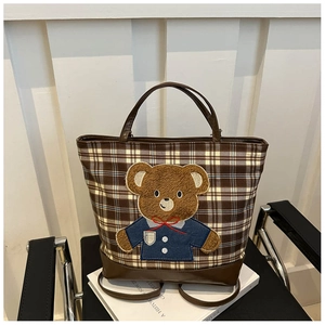 Close-up of plaid tote bag featuring a teddy bear embroidery and brown leather handles