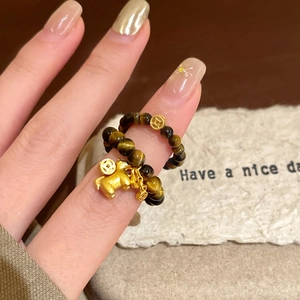 Close-up of tiger eye beaded ring with a golden pig charm and ancient coin pendant
