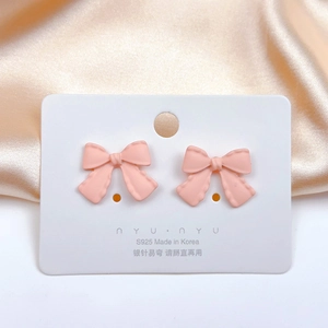 Detail of pink bow-shaped S925 silver needle earrings on display card with satin background