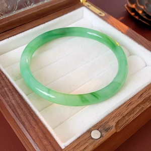 Close-up of a green jade bangle with natural texture in a vintage wooden jewelry box