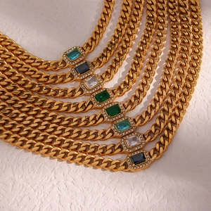 Detail of gold Cuban link necklaces with vibrant emerald, blue, and black rectangle gems