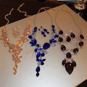 Macro shot of three teardrop crystal necklace and earring sets in gold, blue, and purple