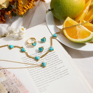 Parure de bijoux dorés avec turquoise en cœur sur livre avec fleurs et orange