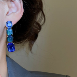Detail of square-cut gradient blue rhinestone earrings on model's ear for luxury set