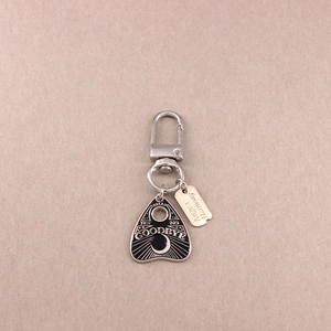 Silver alloy planchette keychain with moon and sun engravings on a beige background
