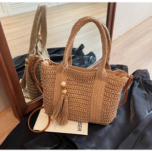 Detailed macro view of khaki woven straw tote bag with decorative tassels and wooden beads
