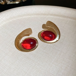 Detail of vintage style gold oval earrings with clear red resin gemstones on beige surface