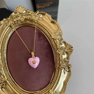 Detail of pink enamel heart pendant with a small gold heart set in an ornate vintage frame