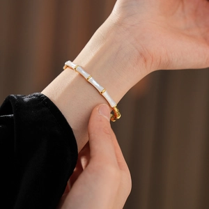 Close-up of bamboo style gold plated bracelet with white enamel on a female wrist