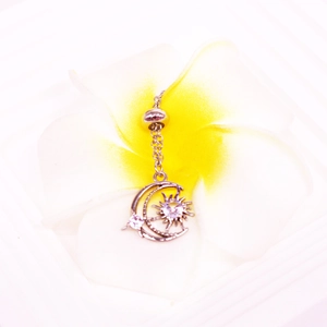 Macro detail of silver moon and sun belly ring with clear cubic zirconia on plumeria flower