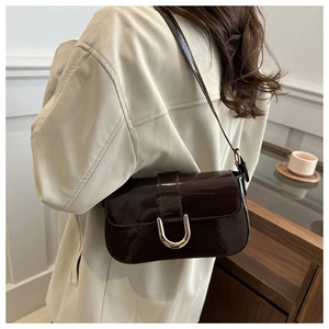 Detail of dark brown patent leather bag with a gold horseshoe buckle on the side