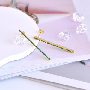 Macro shot of 925 silver needle bar earrings with green zircons on gold metal