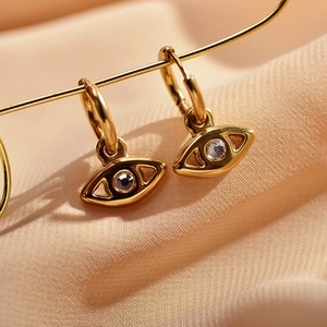 Macro shot of gold Evil Eye hoop earrings with blue zircon on champagne silk fabric