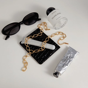 Flat lay of gold chunky chain necklace with perfume and accessories on white surface