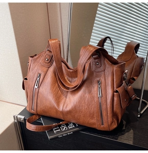 Detailed view of warm brown faux leather tote with functional zippers on a black desk