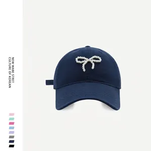 Detail view of the navy blue baseball cap featuring pearl bow decoration and cotton twill