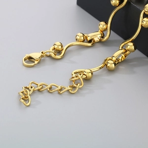 Detailed view of golden wave chain bracelet with metal beads and heart charm