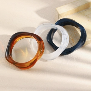 Three acrylic bangles in amber and marble white on a beige stone surface with shadows