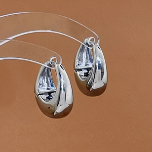Macro shot of silver teardrop hoop earrings on clear stands with high-polish finish