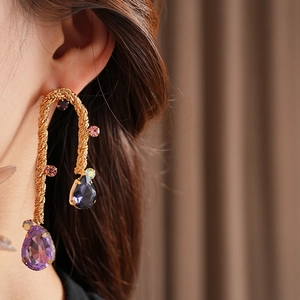 Close-up of vintage gold woven earrings with purple teardrop crystals on a model