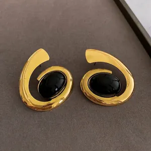 Vintage style gold spiral earrings with oval black stones on a grey textured background