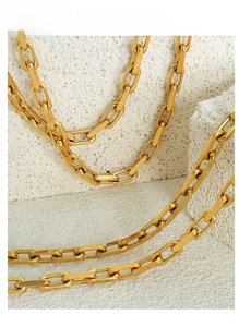 Macro view of polished golden paperclip chain necklace on a minimalist stone base