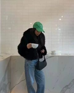 Détail d'une veste en fausse fourrure noire duveteuse avec casquette verte et jean bleu au café