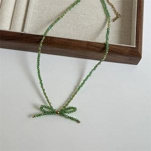 Detail of green beaded necklace featuring a hand-woven bow pendant and gold accents