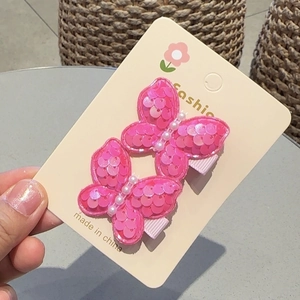 Detail of pink sequin butterfly hair clips with pearl accent on a display card