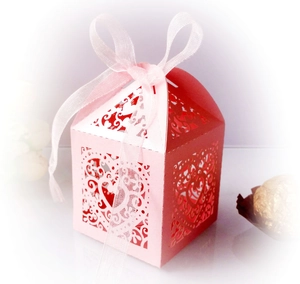 Close-up of pink laser-cut wedding favor box with heart patterns and silk ribbon