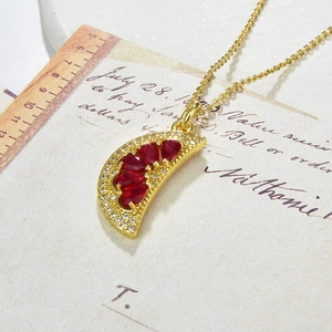 Close-up of gold crescent pendant necklace with red crystals and zircons on vintage paper