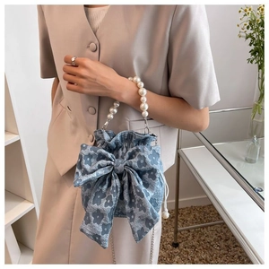 Detail of blue floral drawstring bag with pearl handle and bow accent on model