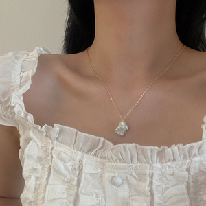 Close-up of minimalist gold chain necklace with a single Baroque pearl on collarbone
