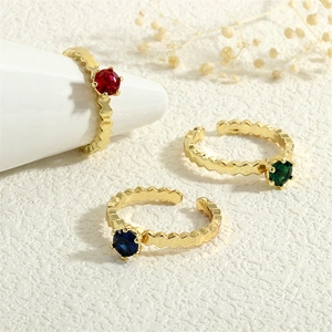 Three 18K gold-plated rings with colorful zircons on a textured white stone surface